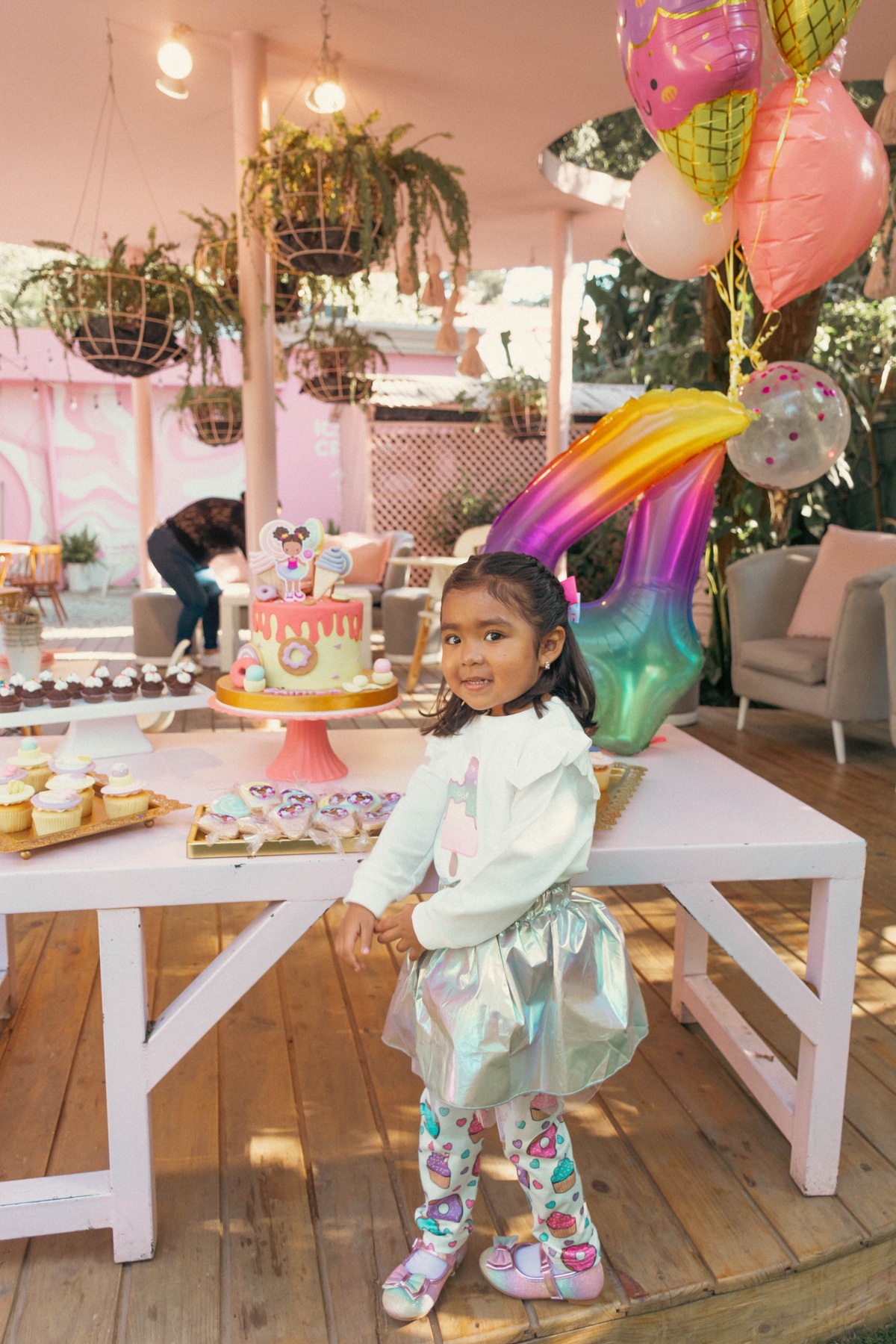 Niña sentada junto a una mesa de cumpleaños con flores y globos