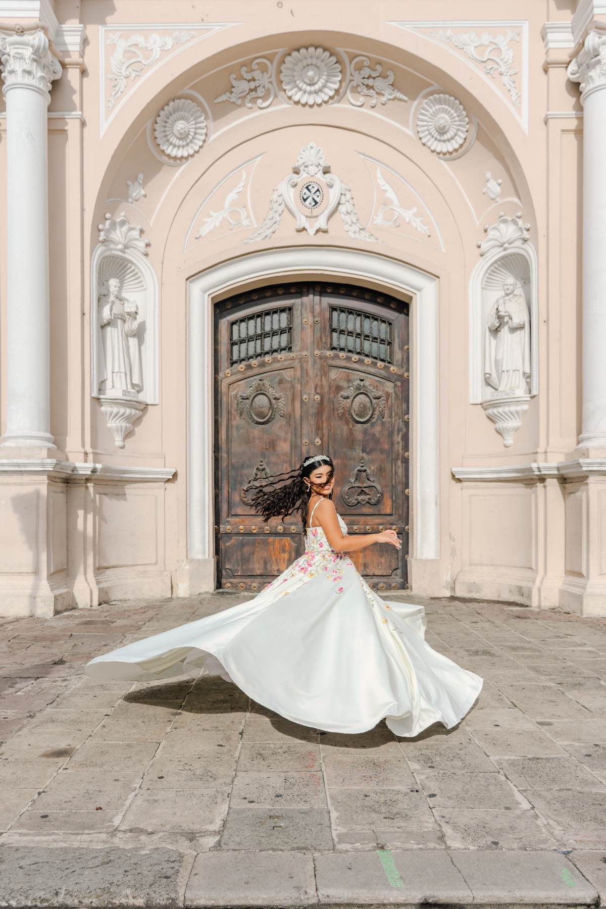 Joven girando con un vestido blanco frente a la entrada de una iglesia