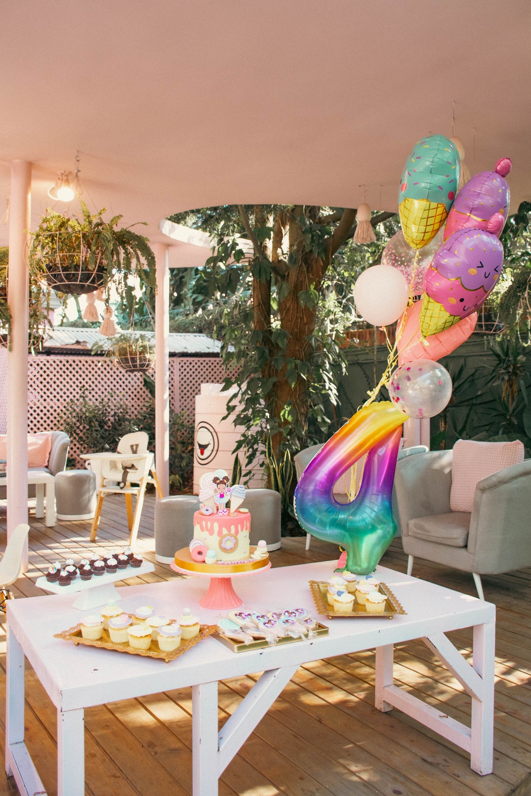 Mesa de cumpleaños con pastel, flores y globos de colores en un jardín