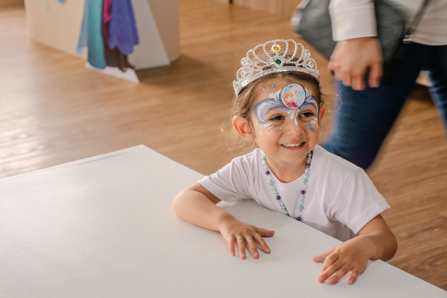 Niña con una corona y pintura de colores en el rostro sonriendo en una mesa